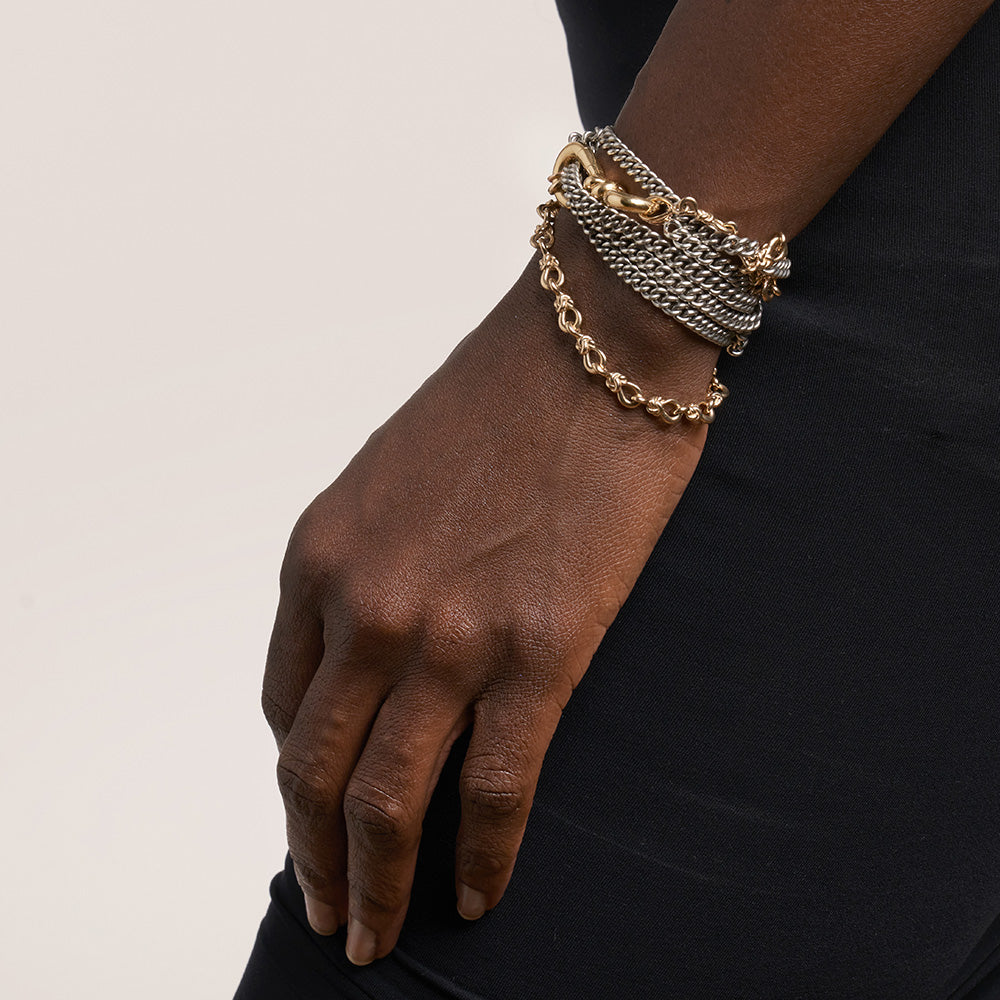 Close up of wrist with many bracelets including chain with knot charm gold