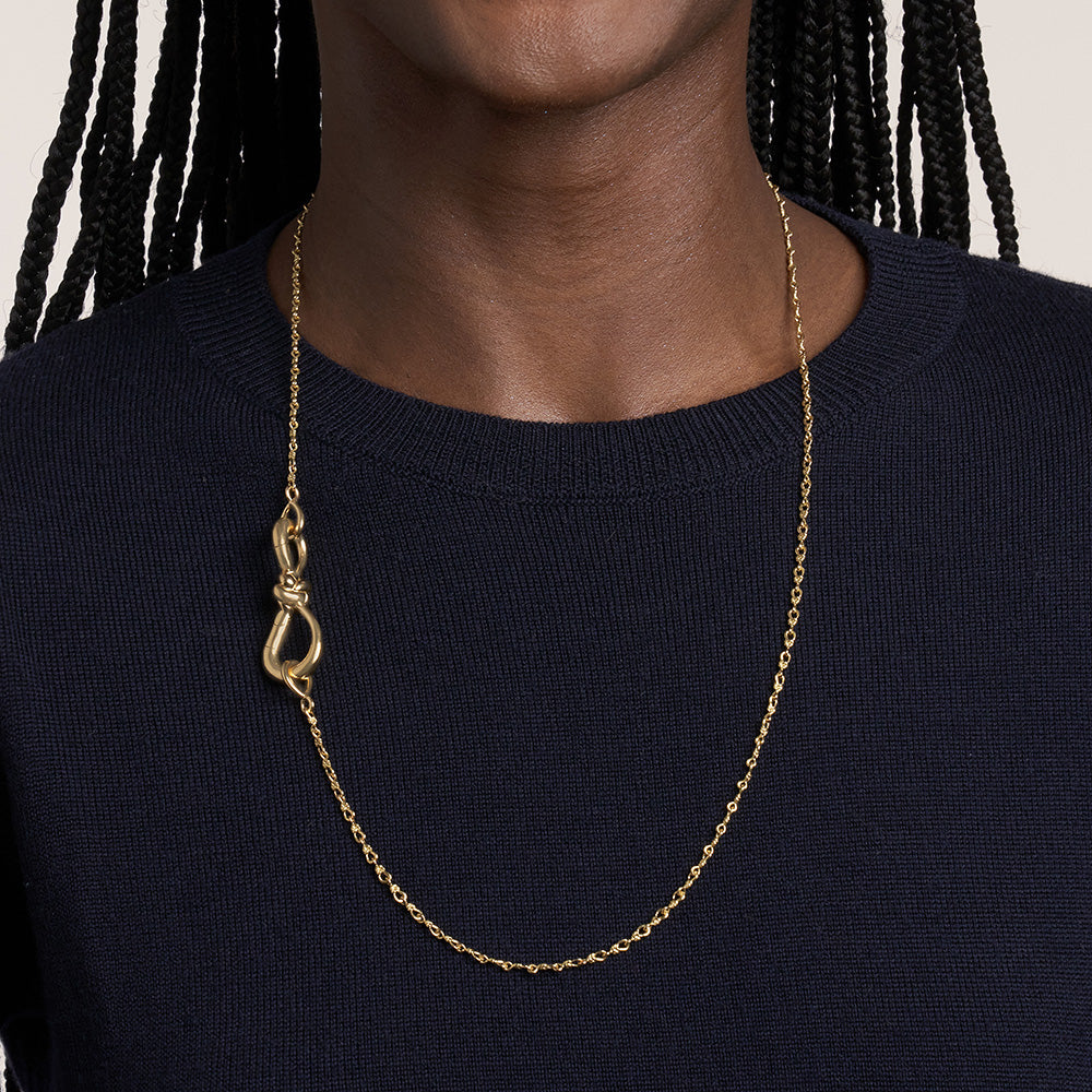 Close up of woman's decolletage wearing gold necklace with knot charm
