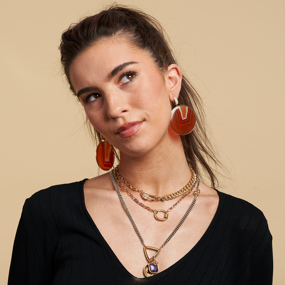 Portrait of woman in black shirt wearing biker chain necklace with beige backdrop