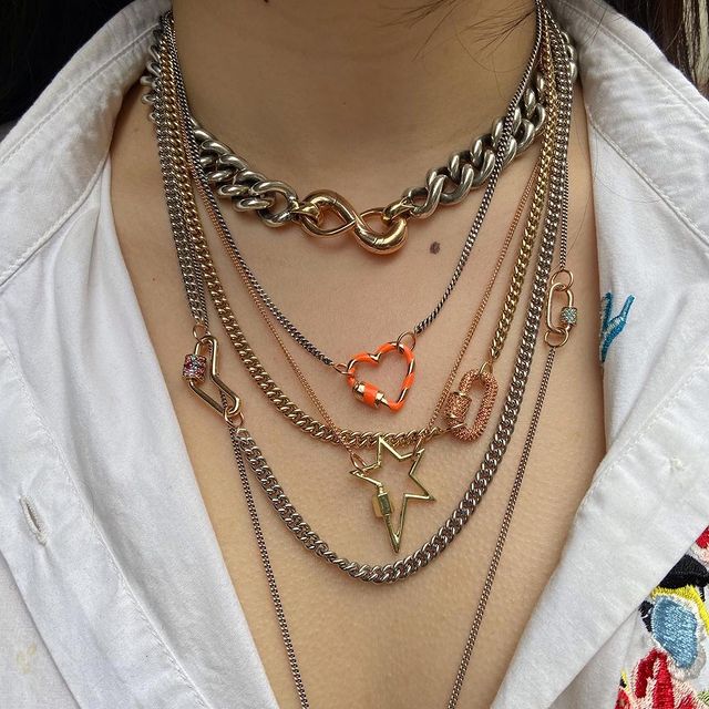 Close up of woman's decolletage wearing many necklaces including thin curb chain necklace