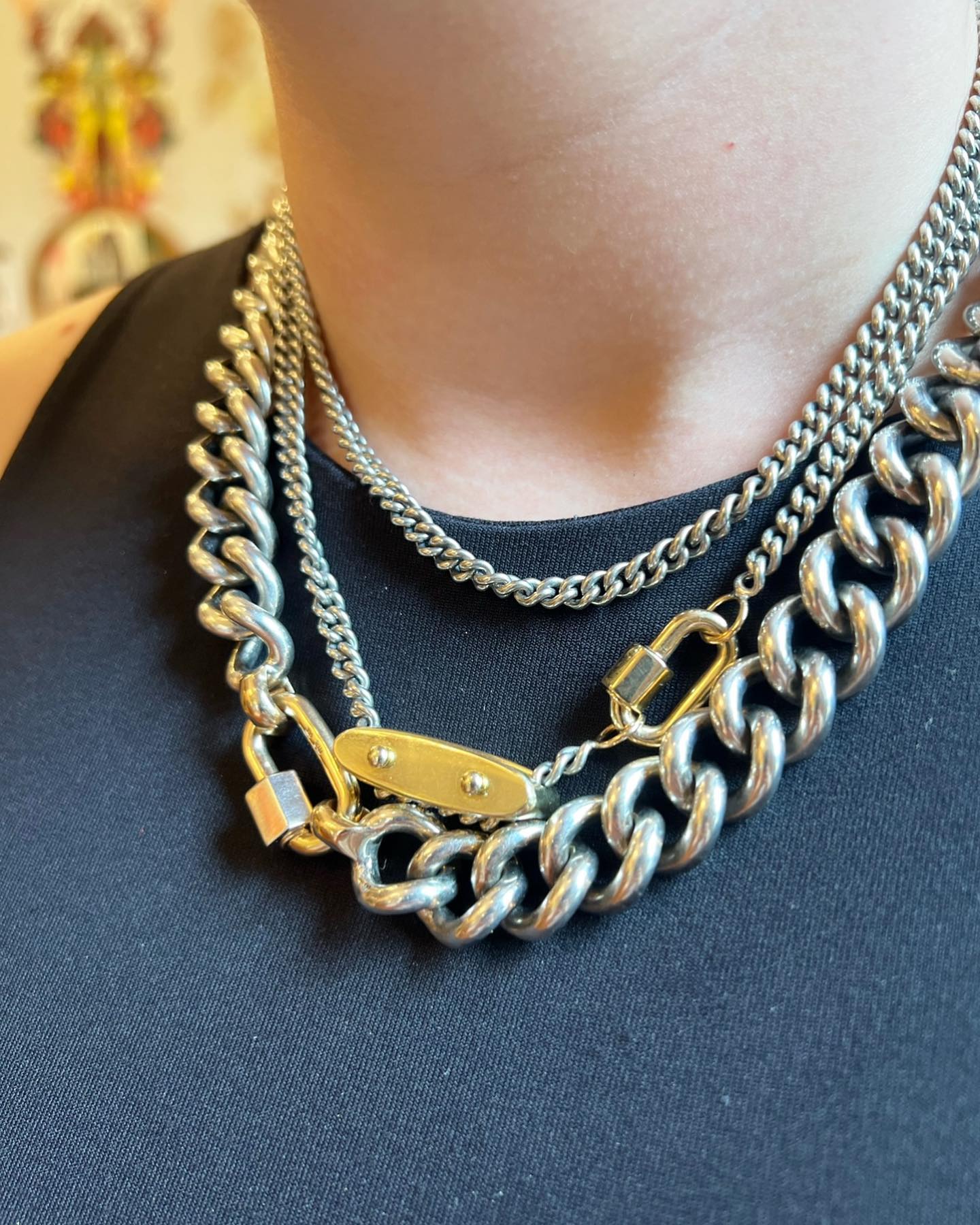 Close up of woman's decolletage wearing multiple necklaces including chunky curb chain necklace silver