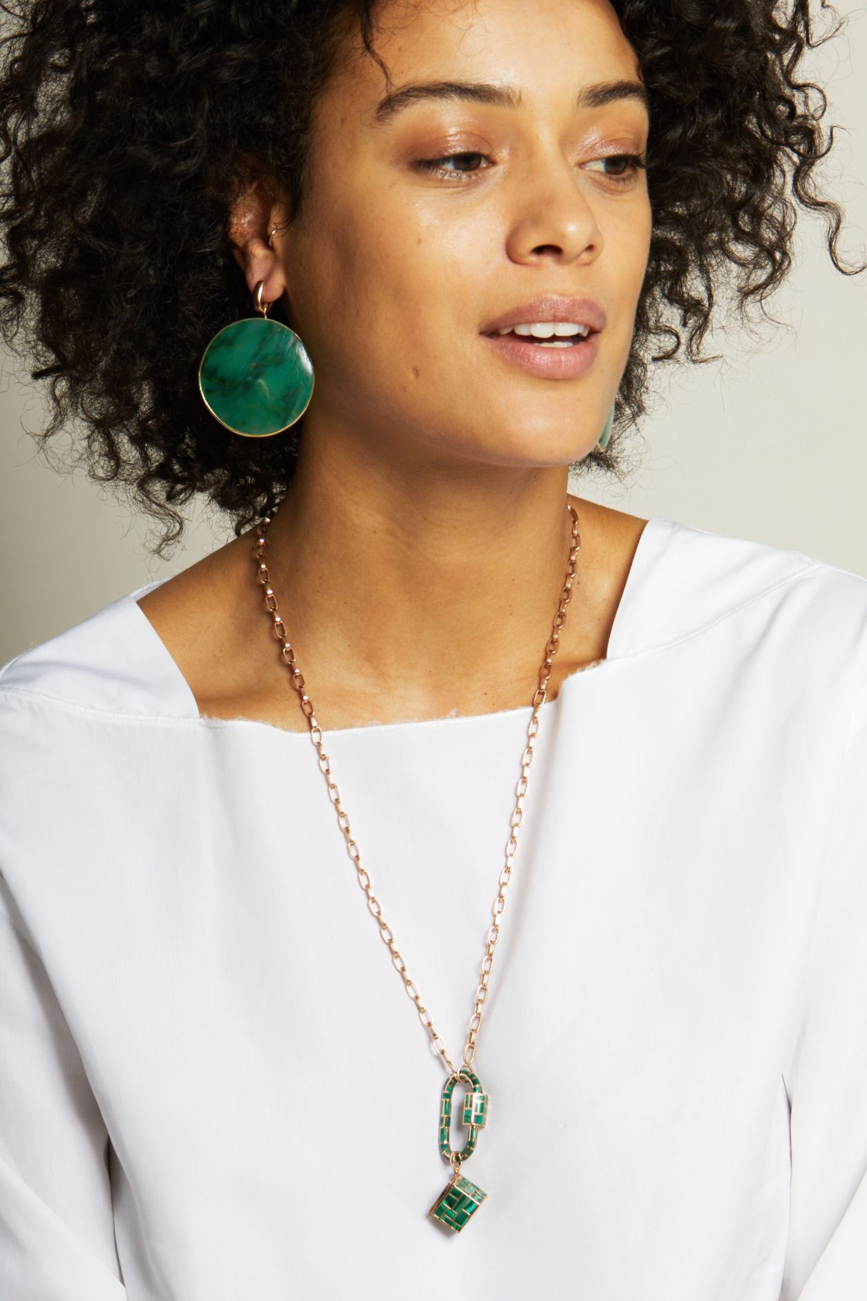 Portrait of woman in white shirt wearing green earrings and rose gold bike chain necklace