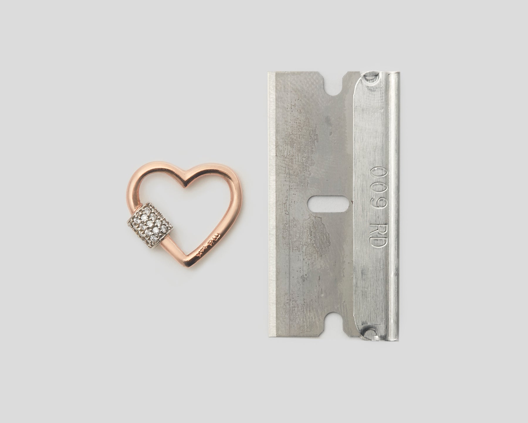 Rose gold diamond heart charm with diamond clasp alongside silver razor blade