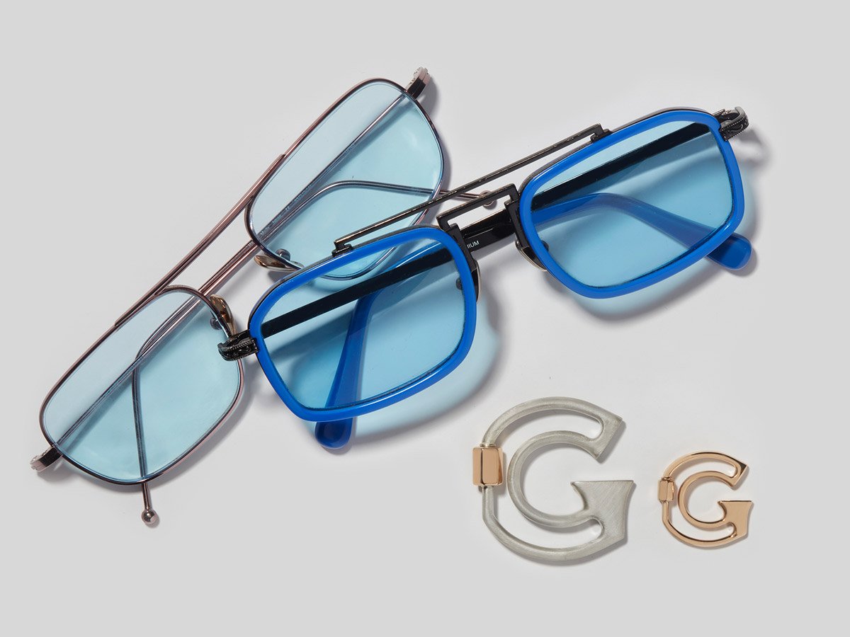 Large silver letter G charm and small rose gold letter G charm alongside two pairs of glasses