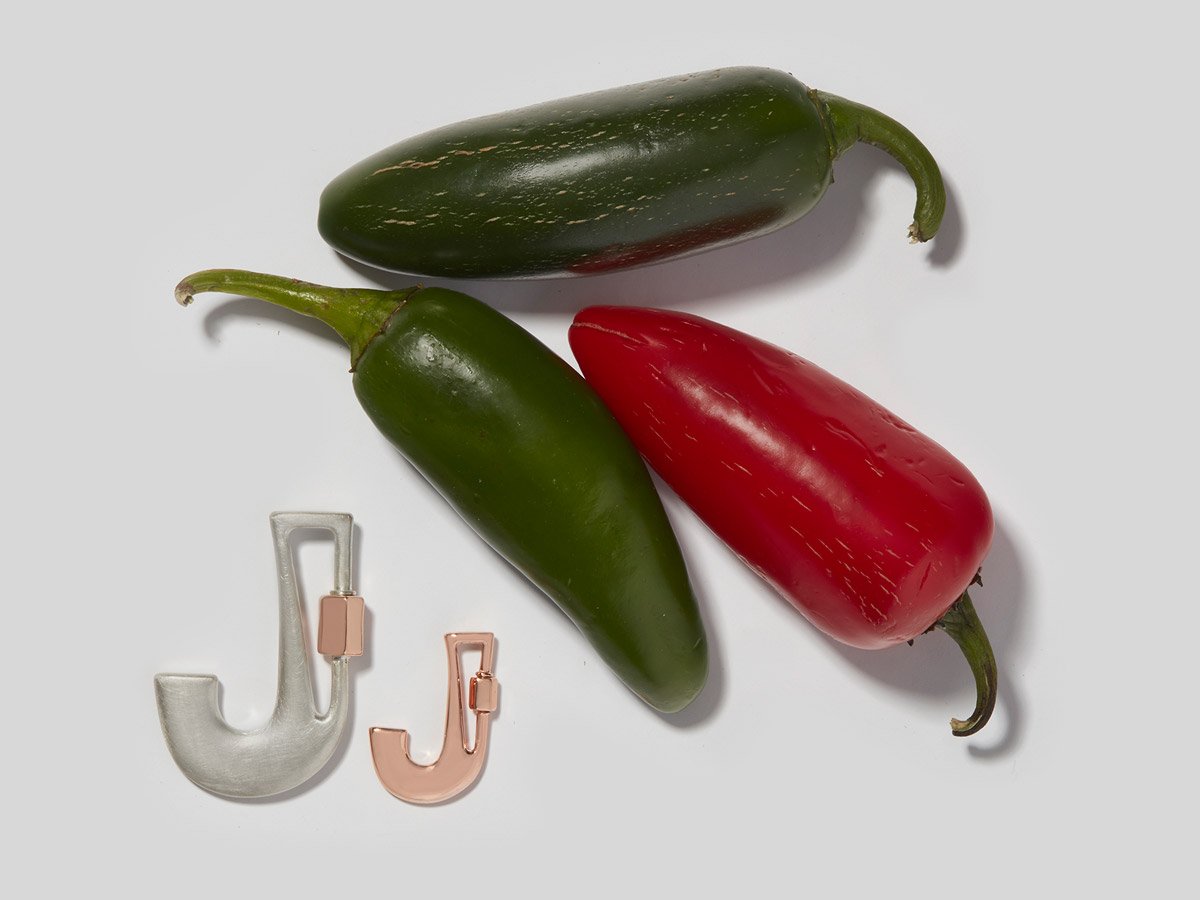 Large silver letter J charm and small rose gold letter J charm alongside pile of jalapeños