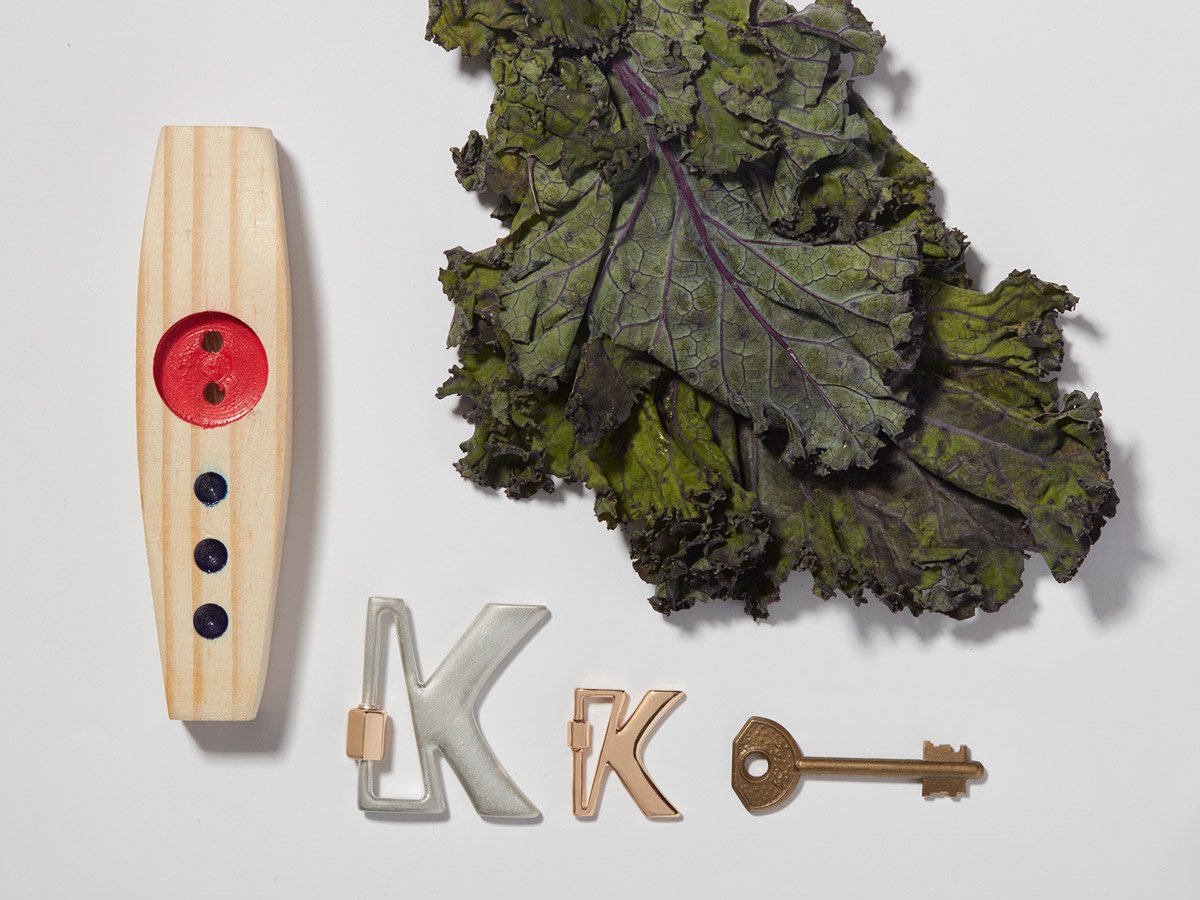Large silver letter K charm and small rose gold letter K charm alongside kale and kazoo