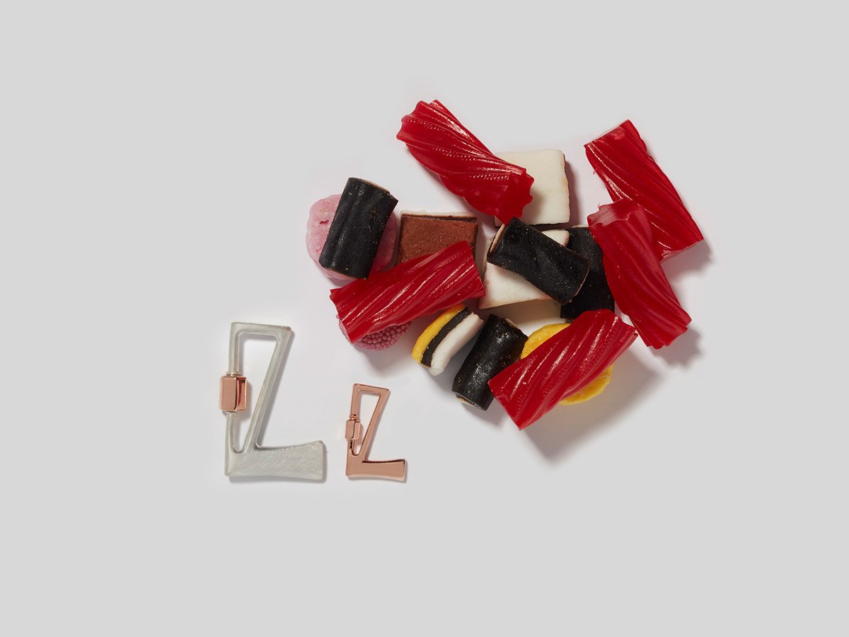 Large silver letter L charm and small rose gold letter L charm alongside pile of licorice