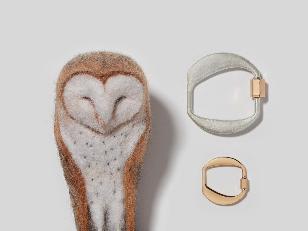 Large silver letter O charm and small rose gold letter O charm alongside small owl plush