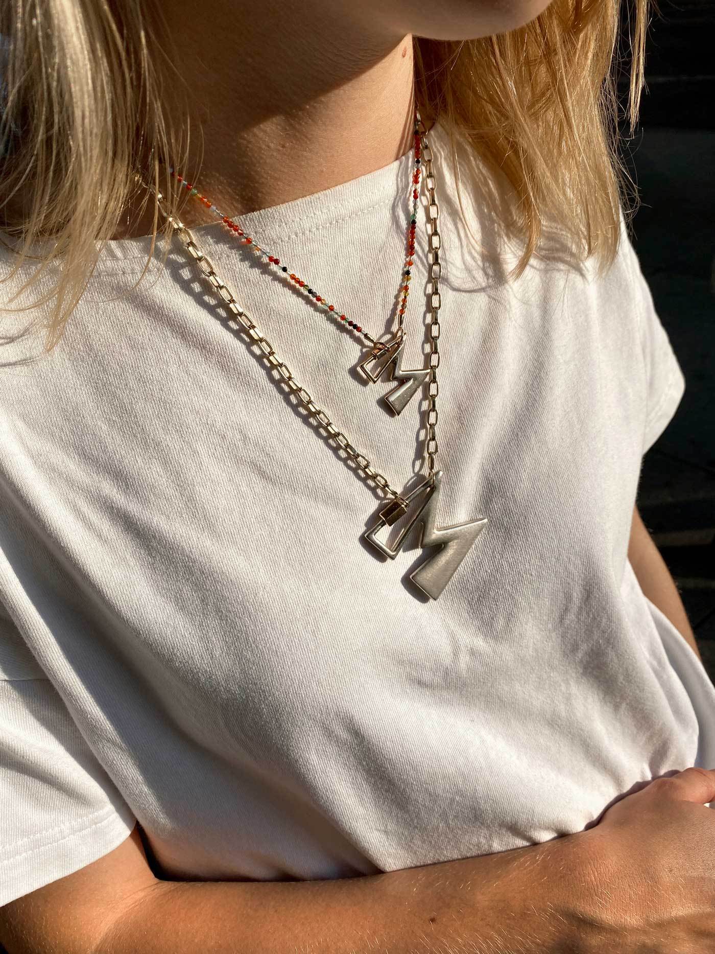 Close up of woman's decolletage wearing two necklaces with M lock