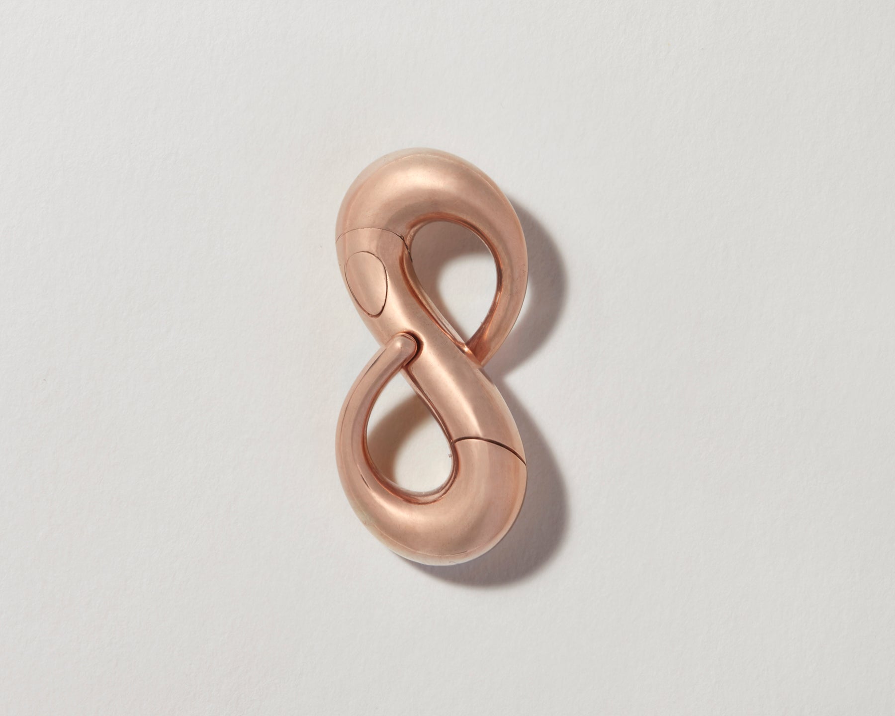 Rose gold infinity lock with clasp closed against gray backdrop