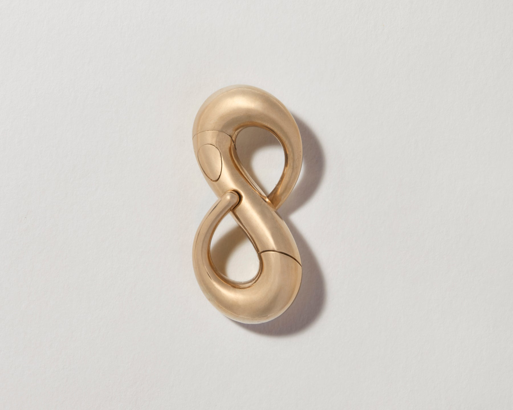 Gold infinity lock with clasp closed against gray backdrop