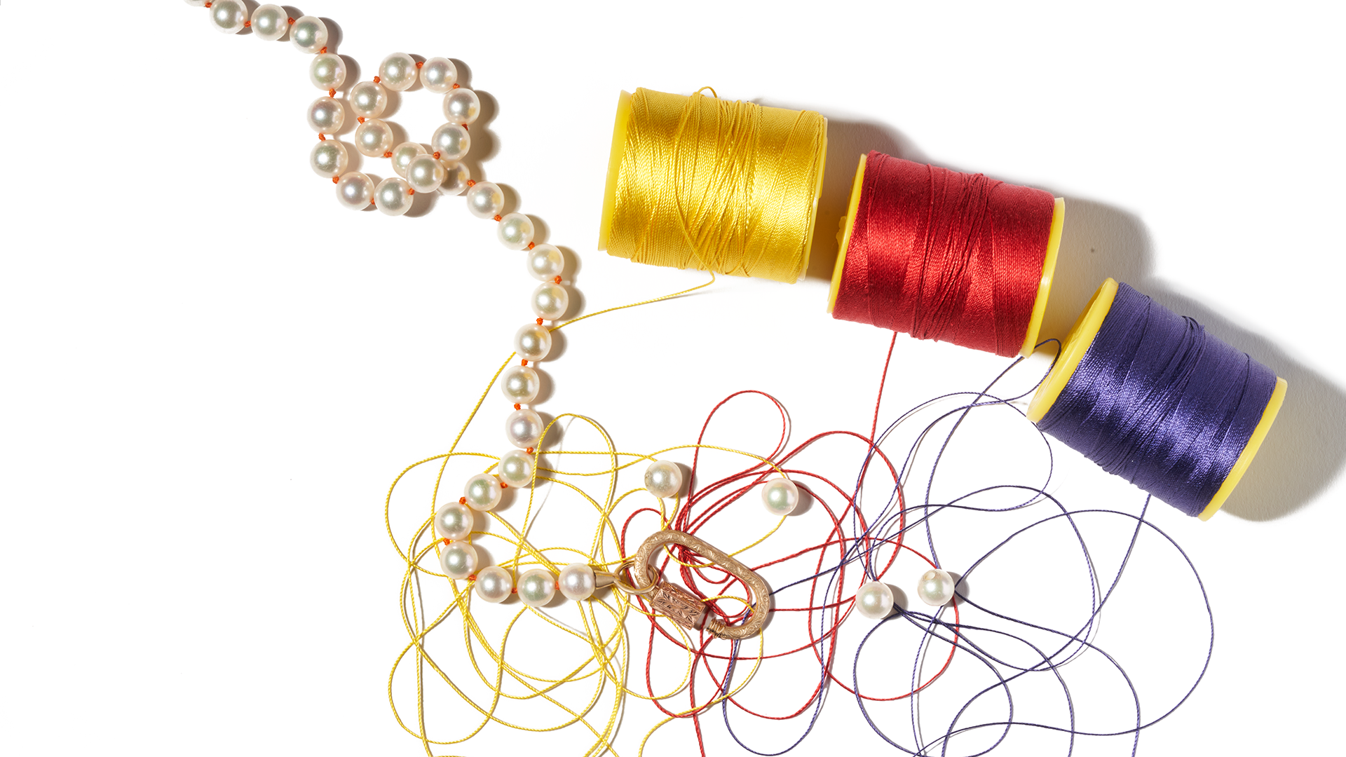 Three spools of thread alongside custom made pearl jewelry strand