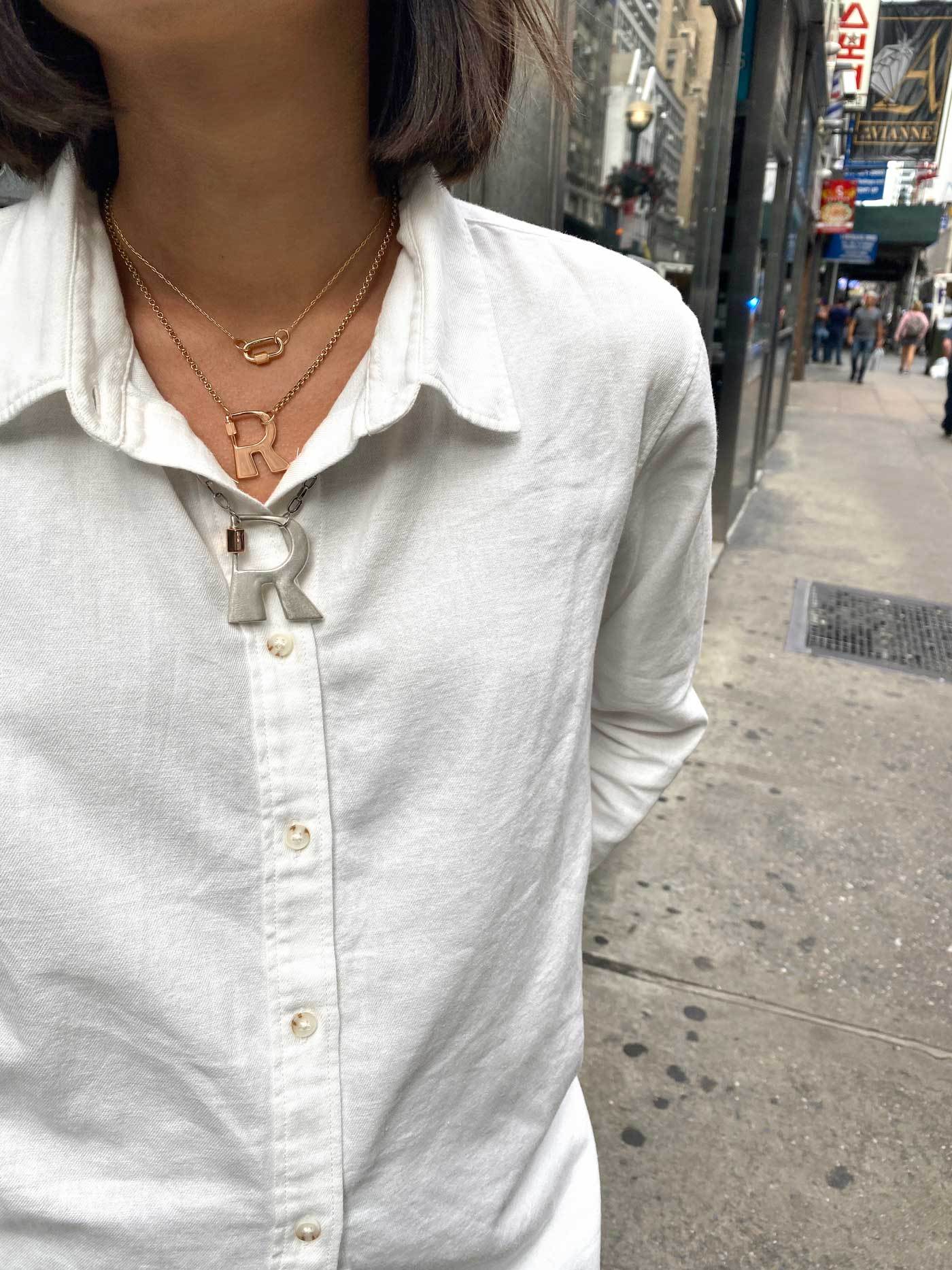 Close up of woman's decolletage wearing two necklaces with R locks