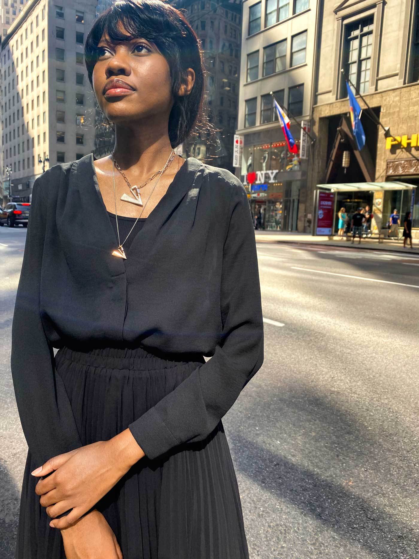 Woman in city street with hands crossed in front of her wearing two necklaces with v lock charms