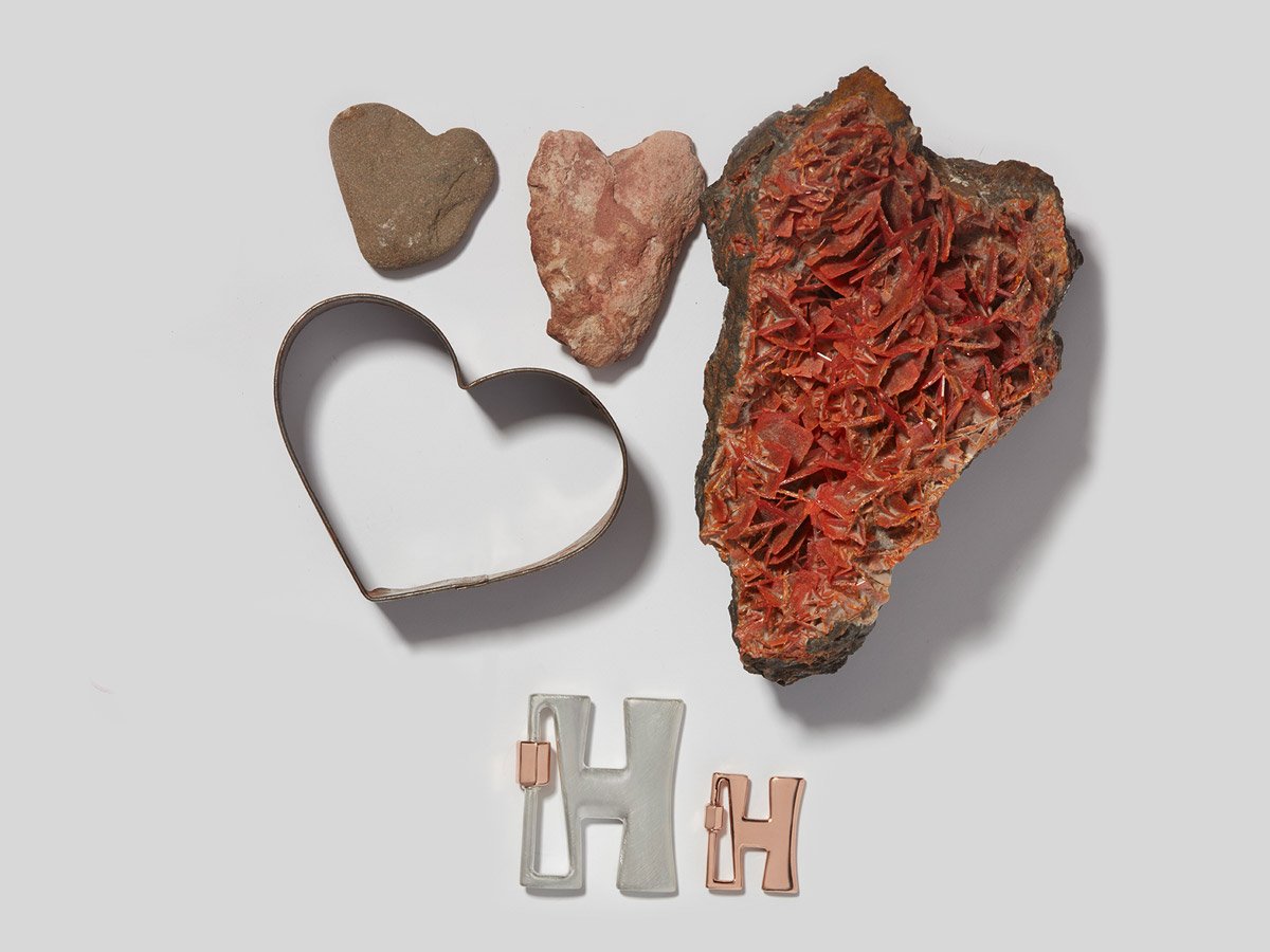 Large silver letter H charm and small rose gold letter H charm alongside various heart shaped objects
