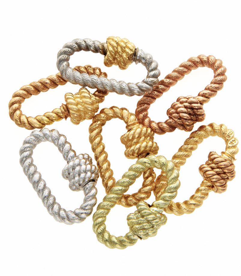 Twisted lock charms of various metals arranged in loose pile against white backdrop