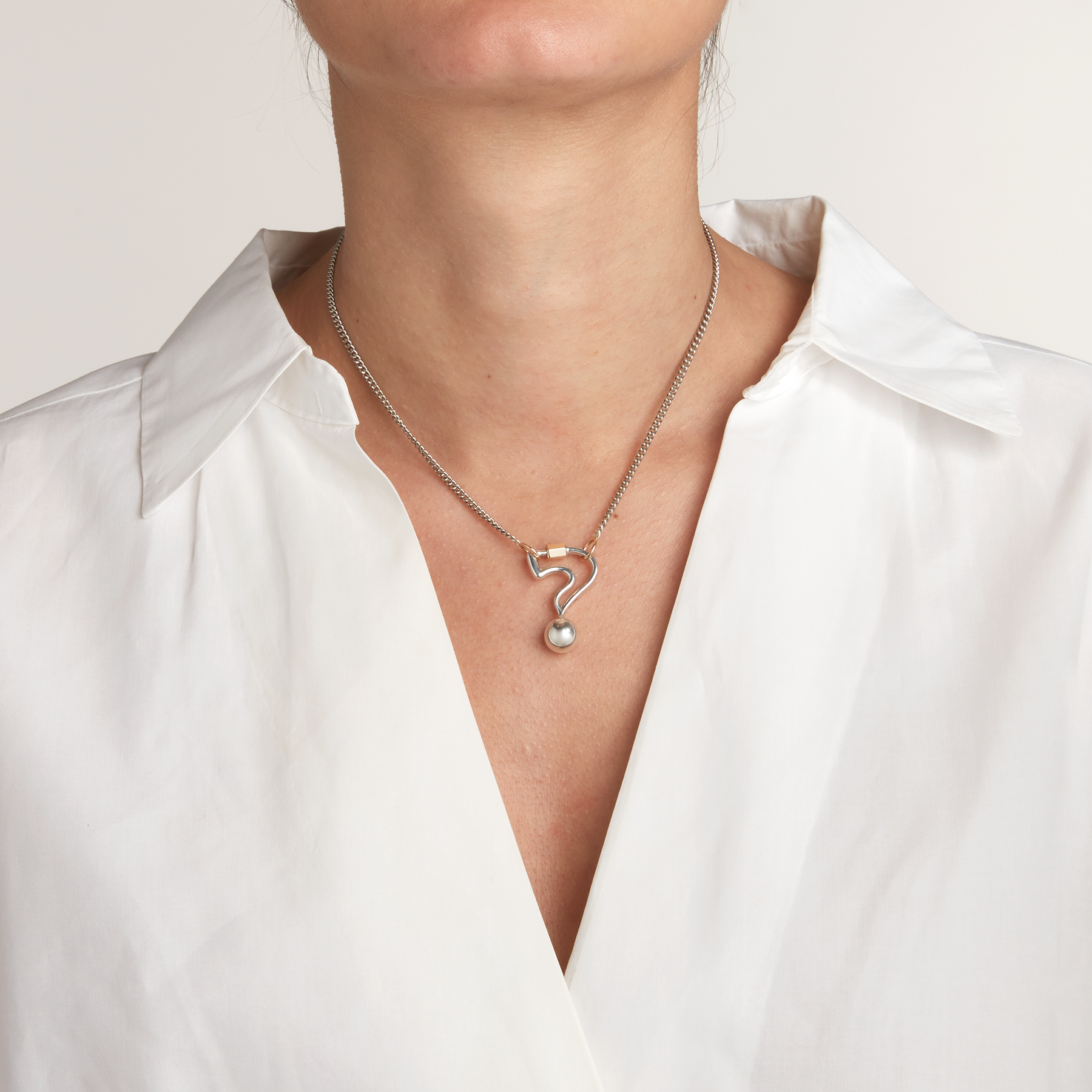 Close up of woman's decolletage wearing silver question mark jewelry