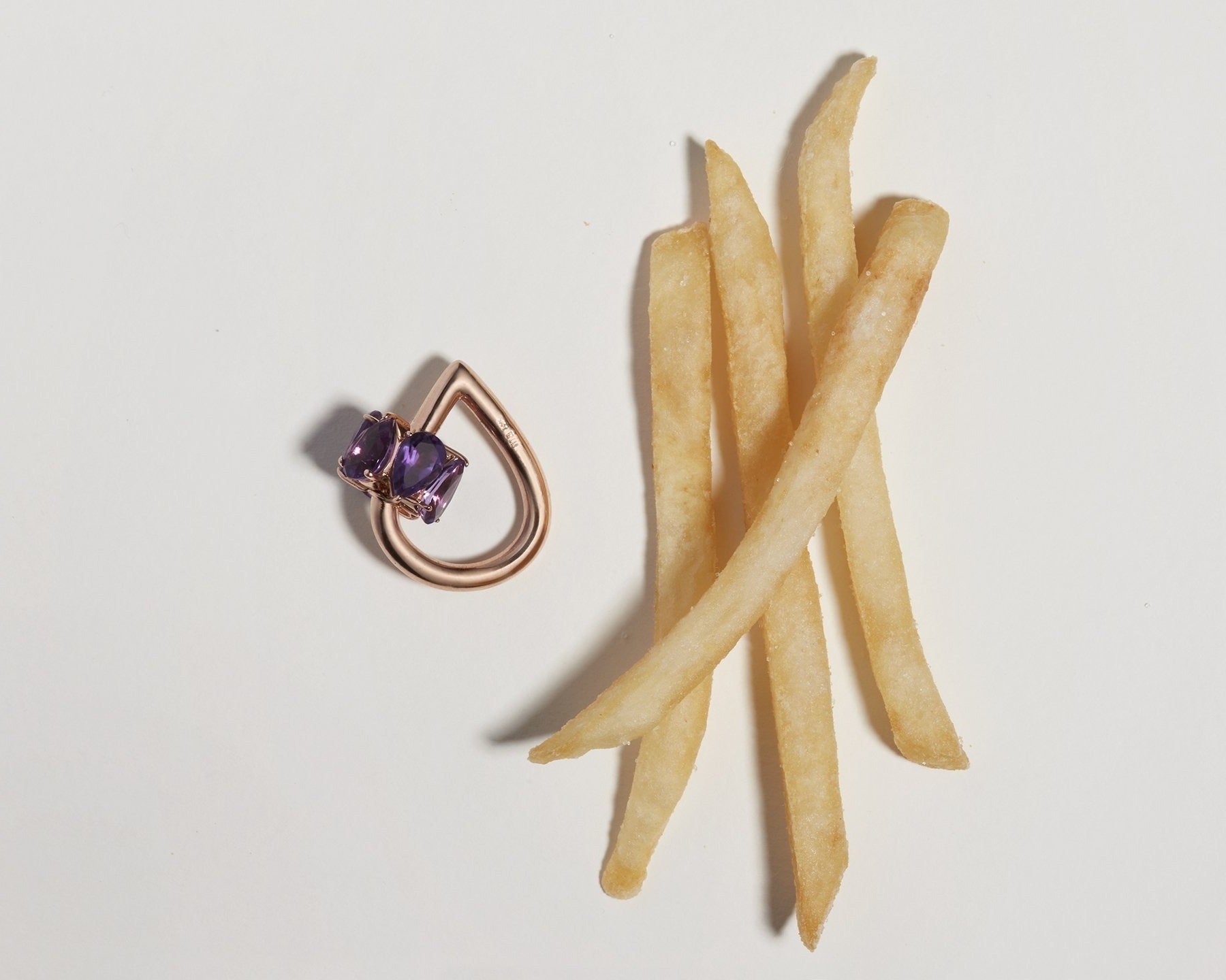 Rose gold droplock charm with purple gemstones alongside four french fries 