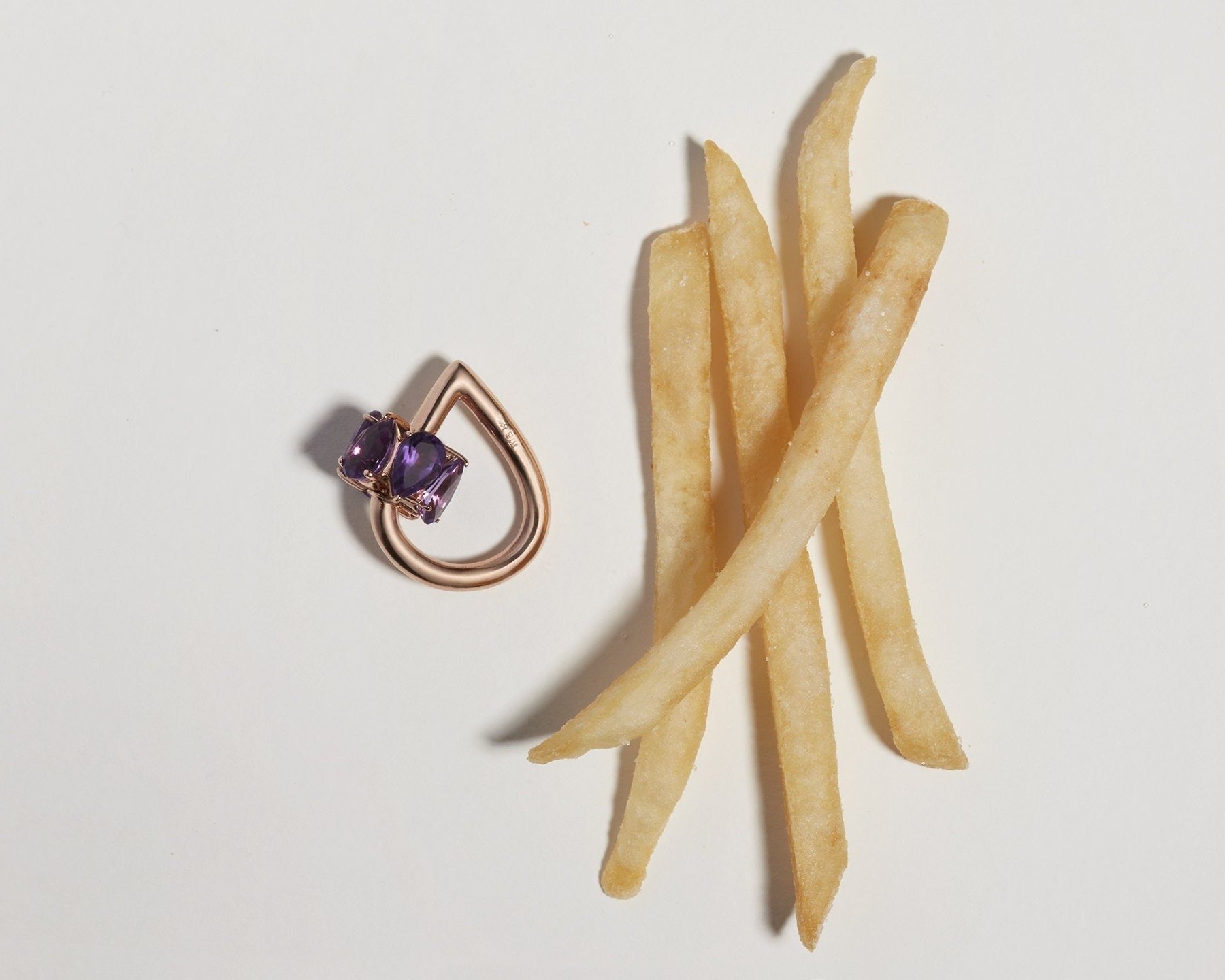 Rose gold droplock charm with purple gemstones alongside four french fries