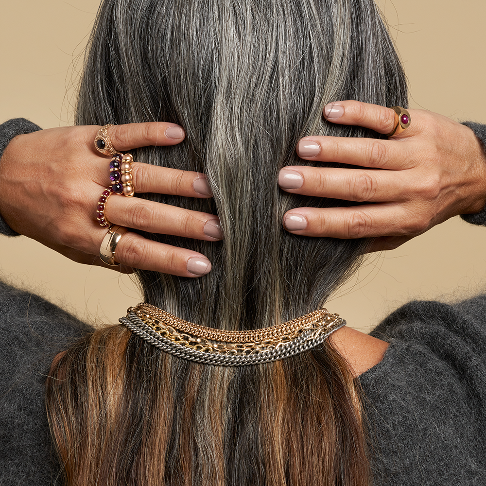 Woman adjusting hair with two hands wearing multiple gold rings with balls