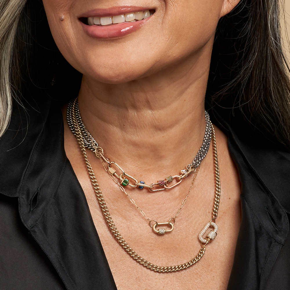 Close up of woman's decolletage wearing multiple necklaces including rolo chain necklace