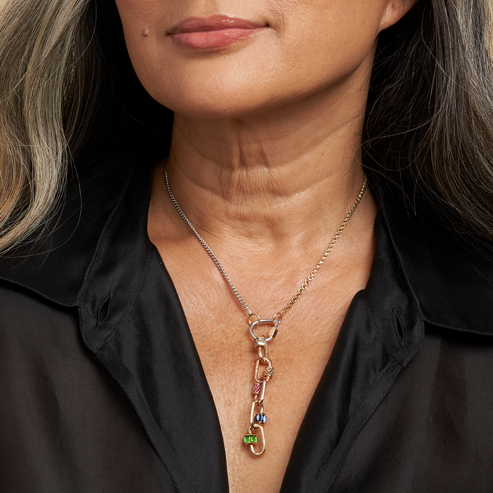 Close up of woman's decolletage wearing gold and silver chain necklace with multiple stoned charms
