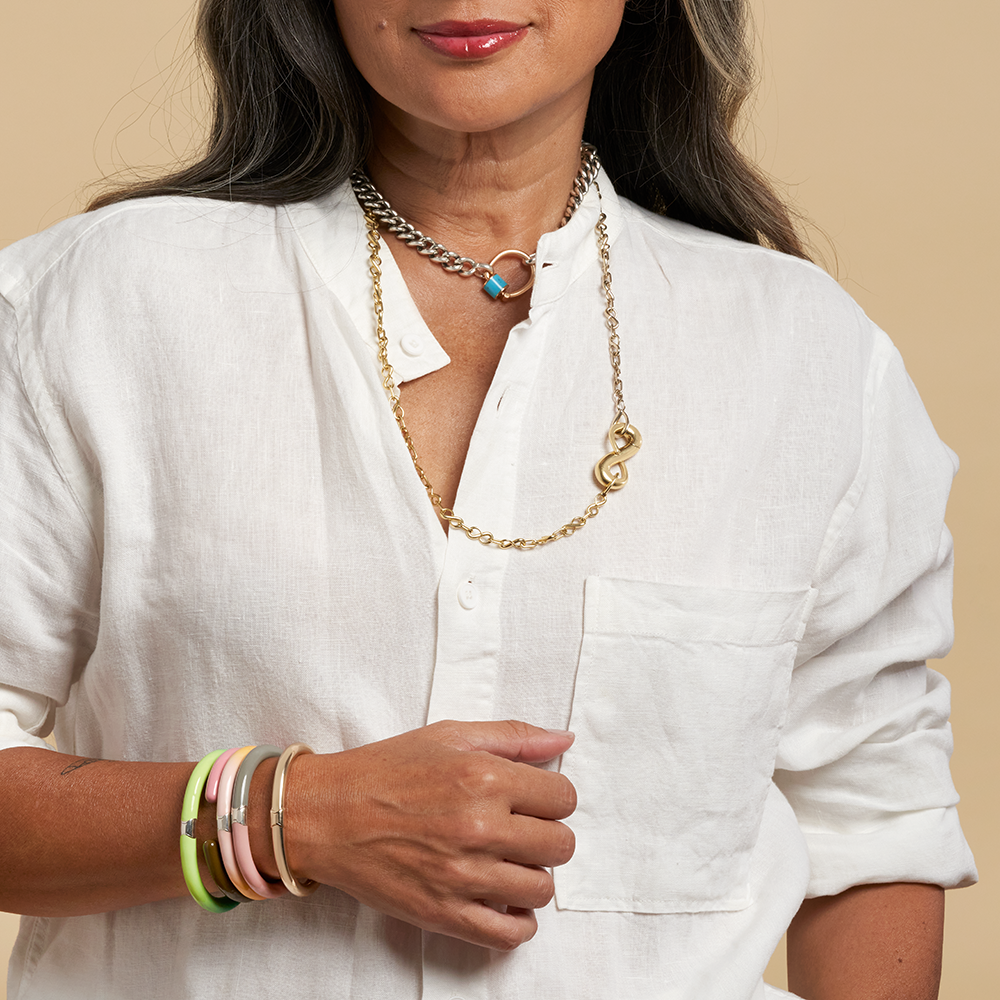 Close up of woman's torso wearing gold necklace with infinity lock charm and white button up top