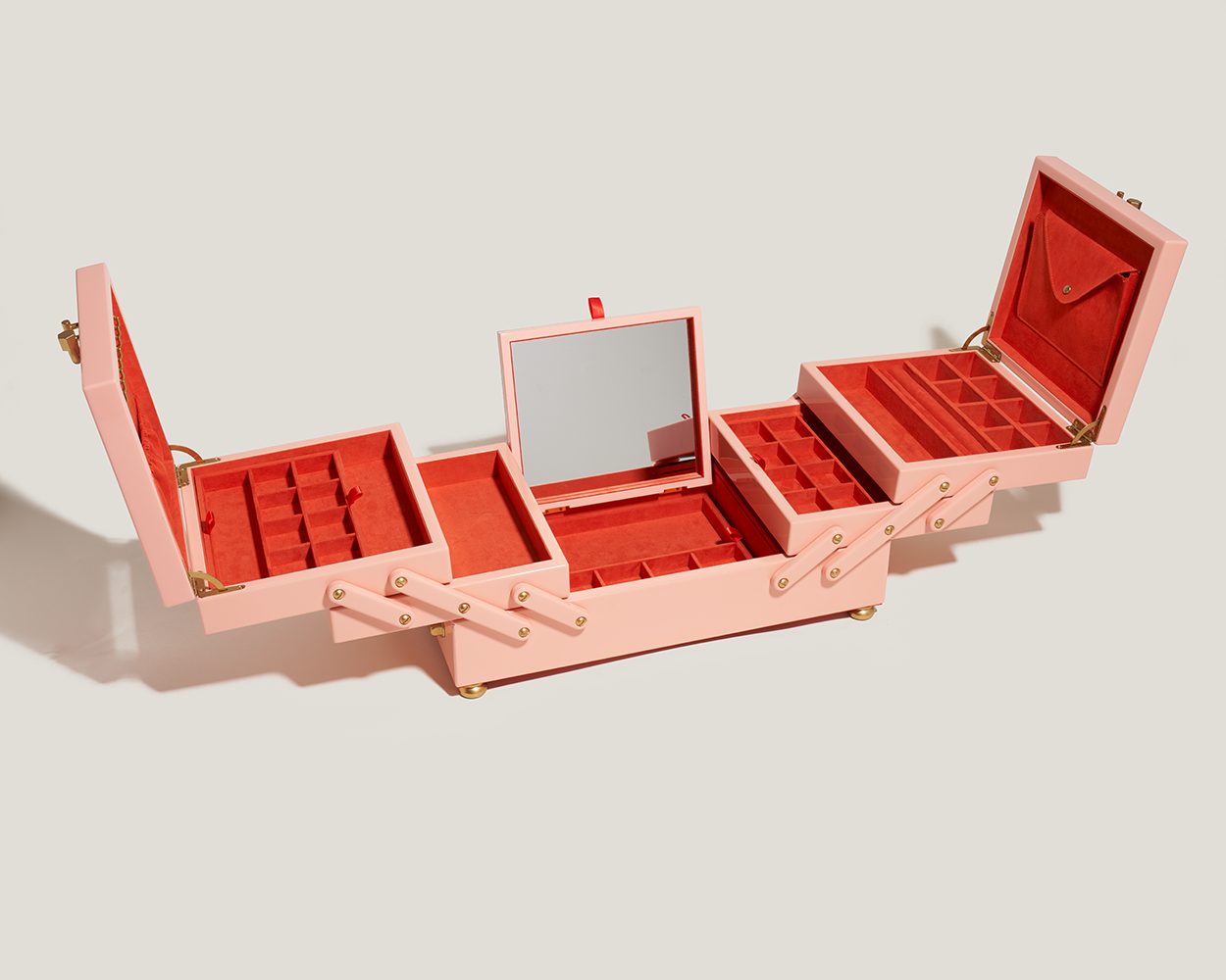 Open pink jewelry box with wooden exterior and red interior and attachment mirror