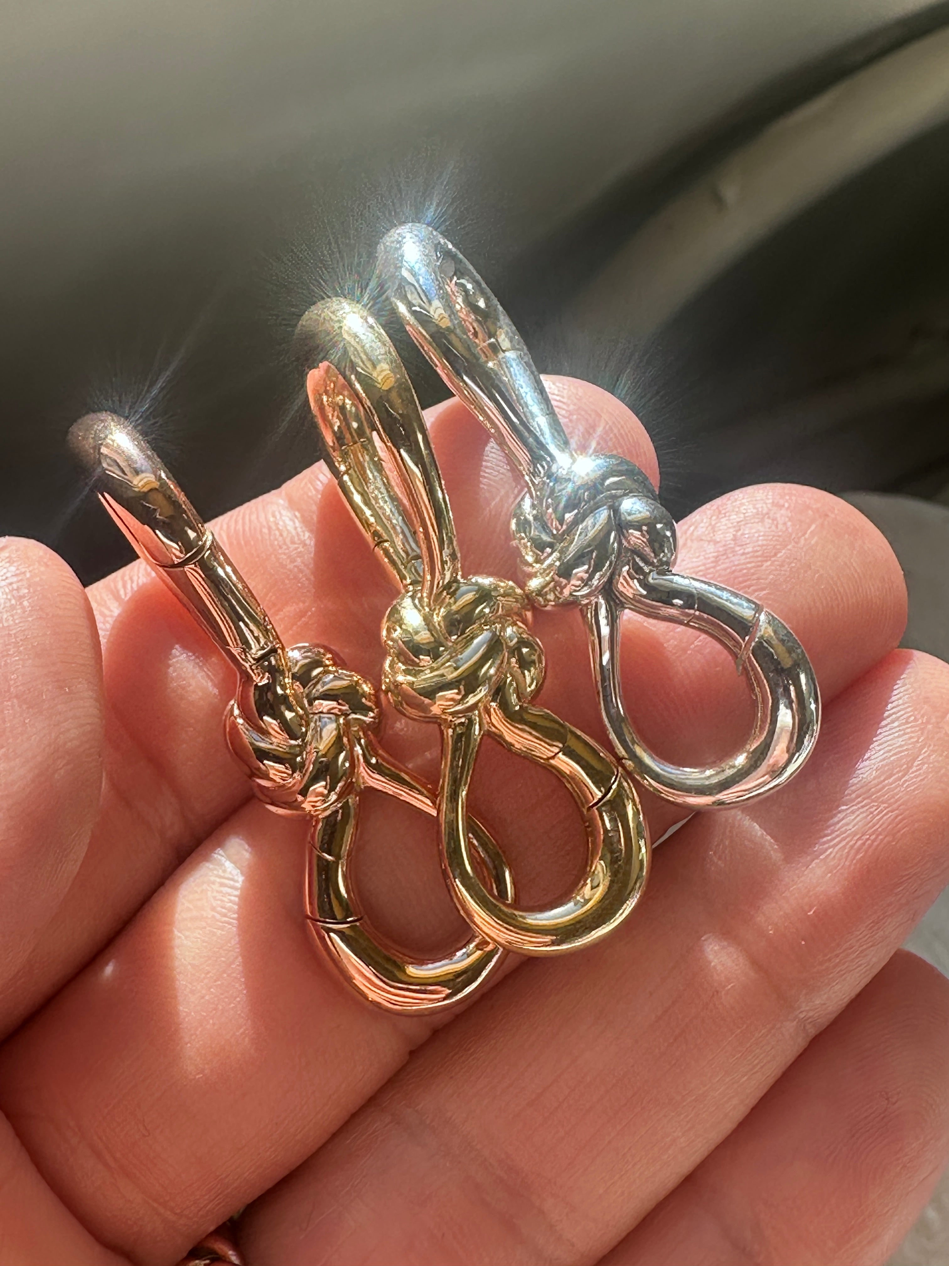 Close up shot of silver, rose gold, and yellow gold knot lock charms in the palm of hand with sunlight shining on them