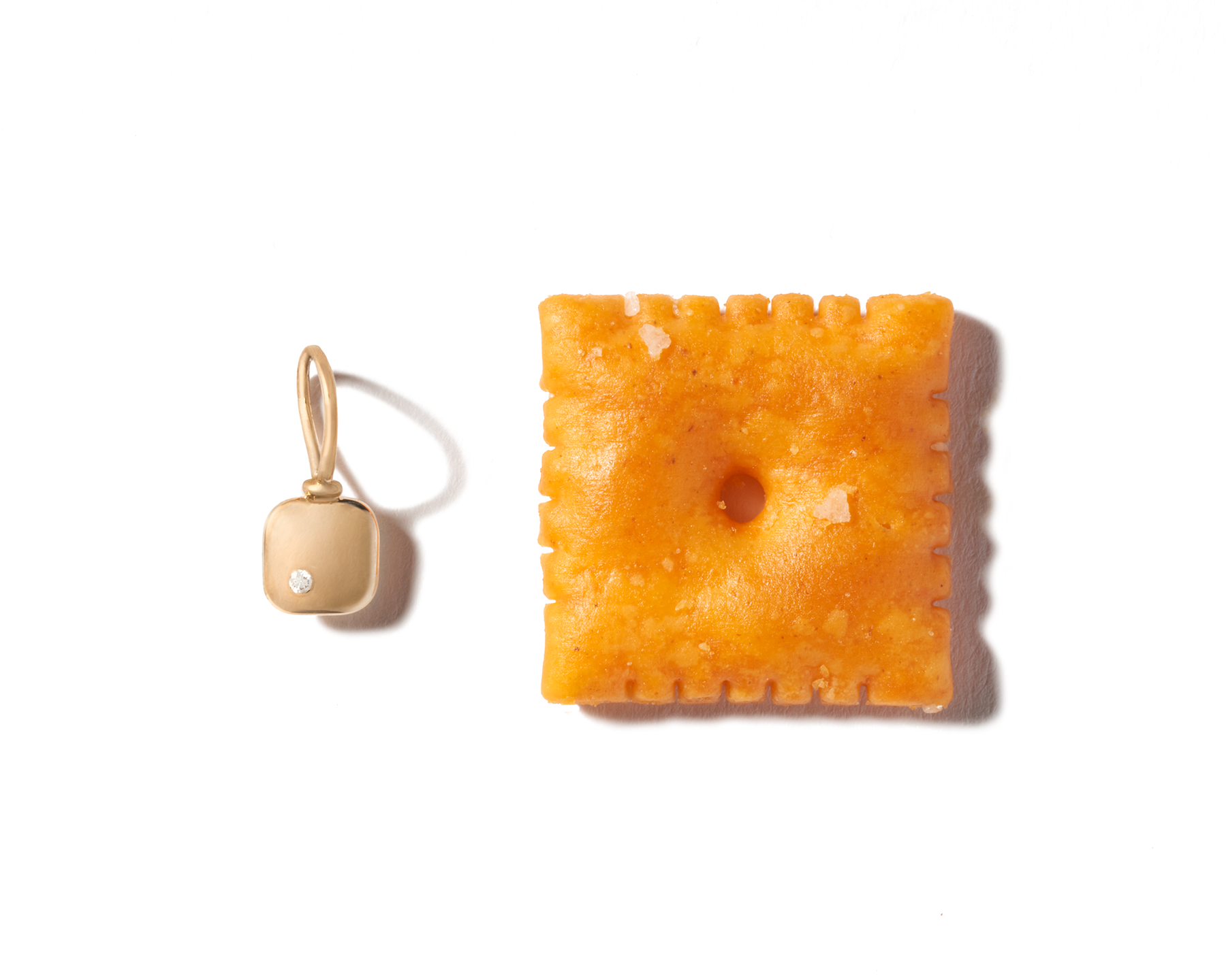 Square tiny gold necklace charm next to Cheez-It