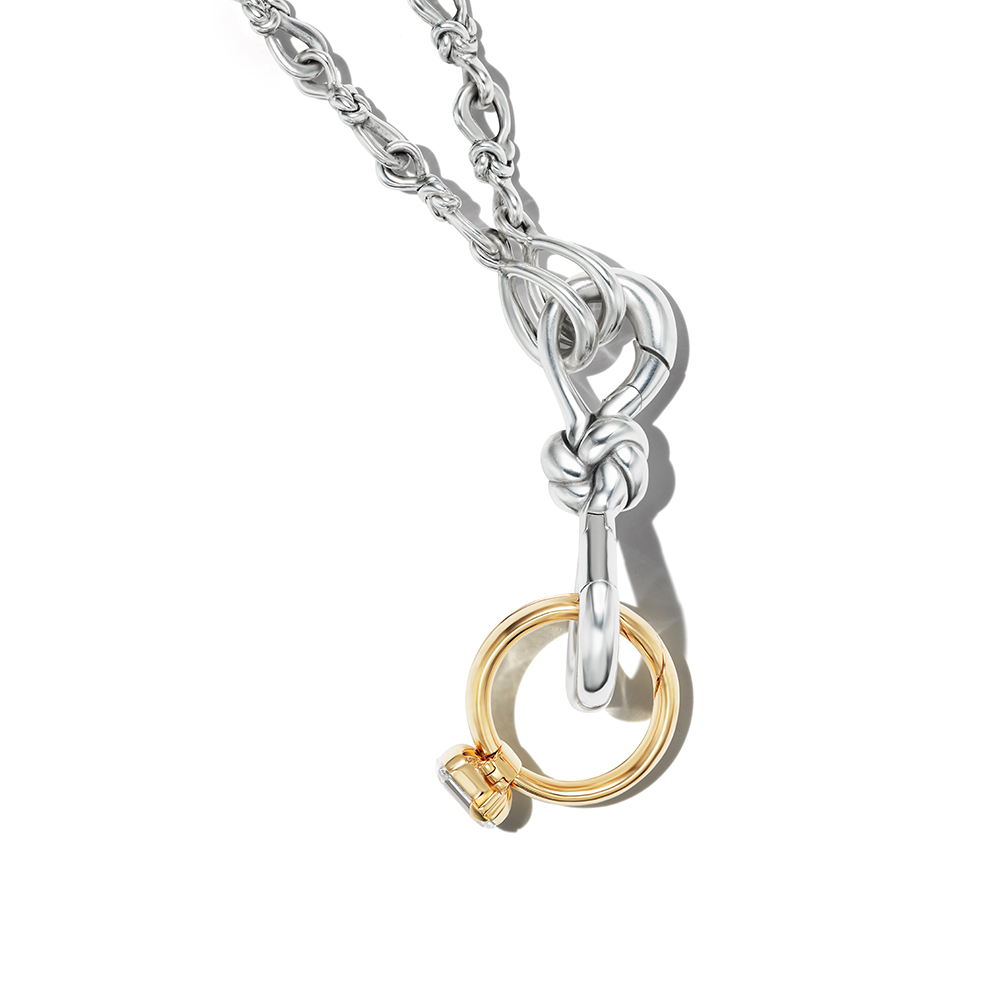 Close up of knot charm silver attached to silver necklace chain and gold diamond ring