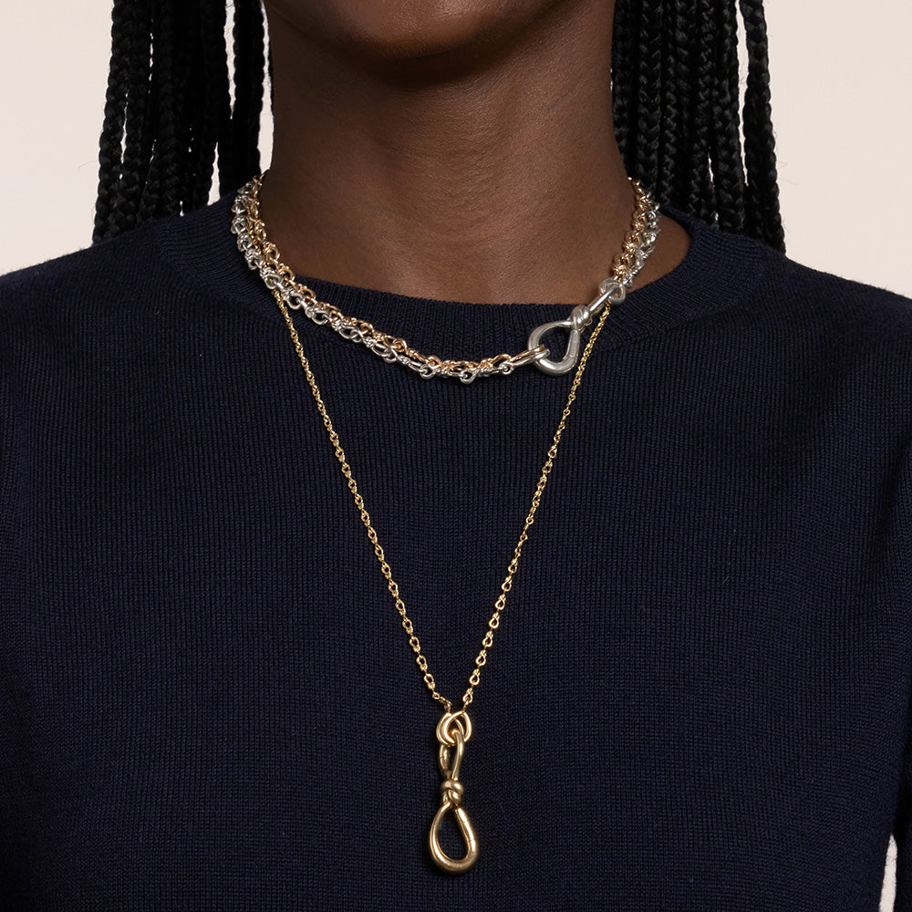 Close up of woman's decolletage wearing two necklaces with silver and gold love knot charms