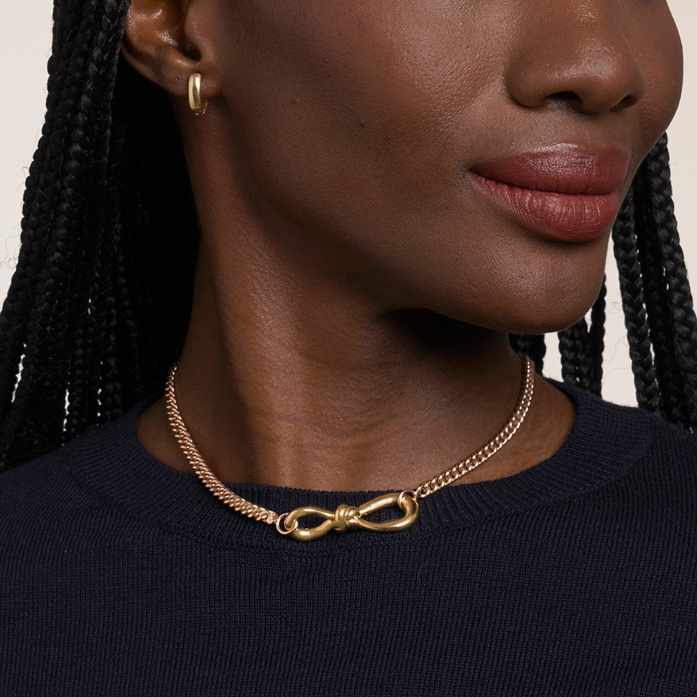 Close up of woman's decolletage wearing short gold love knot charm necklace