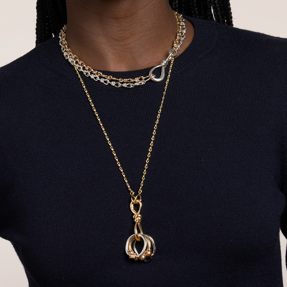 Close up of woman's decolletage wearing two necklaces with knot charm gold and silver