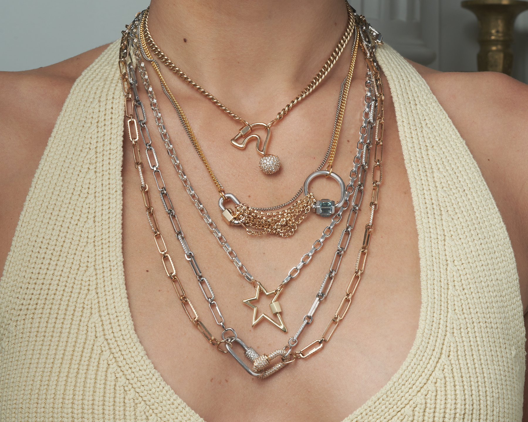 Close up of woman's decolletage wearing multiple necklaces including necklace with diamond lock charm