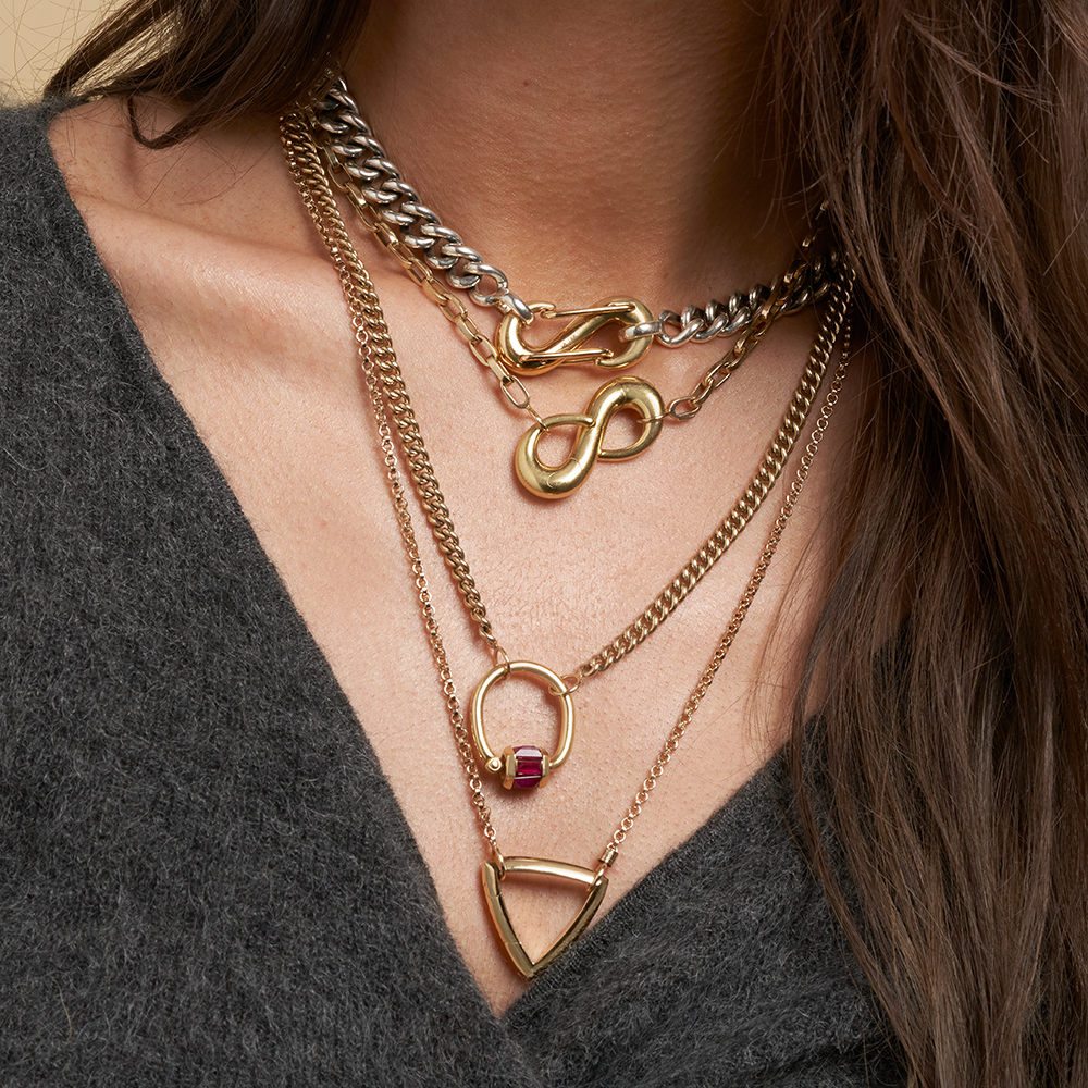 Close up of woman's decolletage wearing many necklaces including neckace with infinity charm