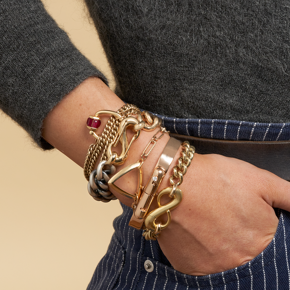 Close up of woman's wrist wearing many bracelets including gold bracelet with silver charm clasp
