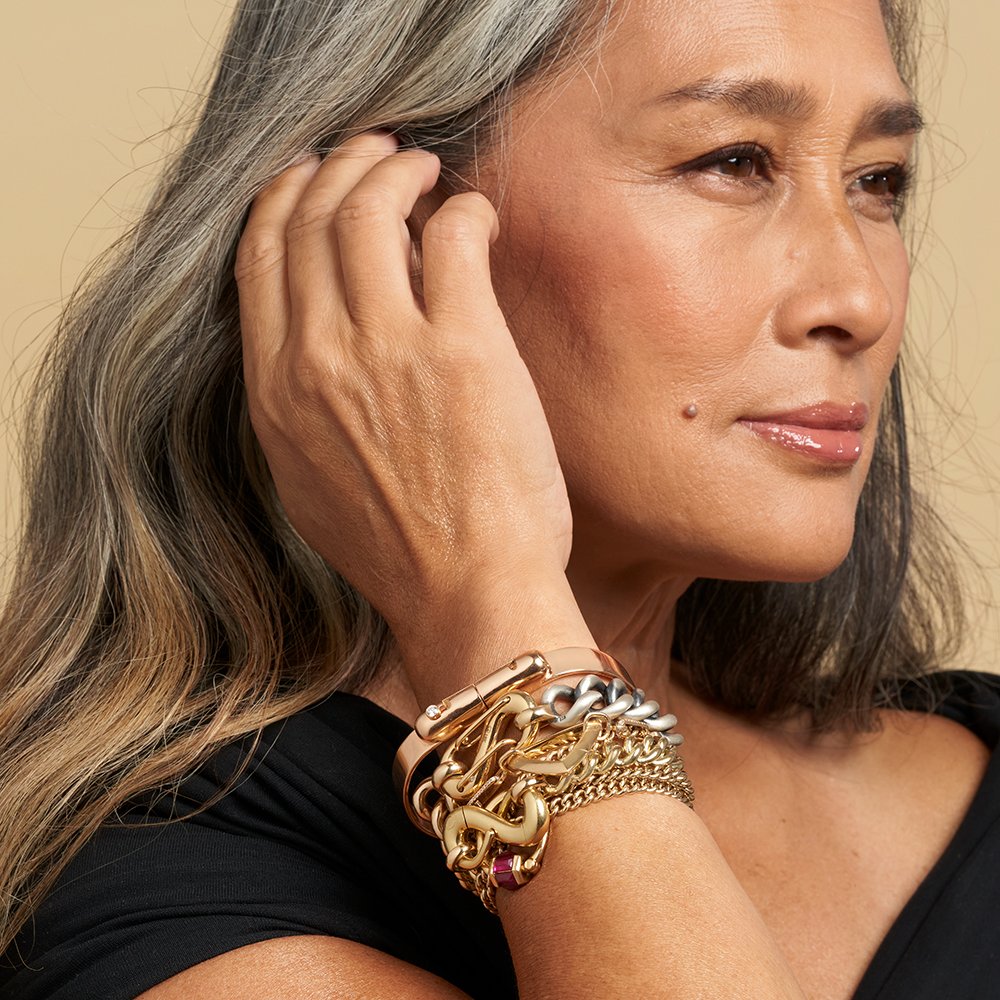 Woman tucking hair behind ear wearing many bracelets on wrist including gold bracelet with silver mechanism lock charm