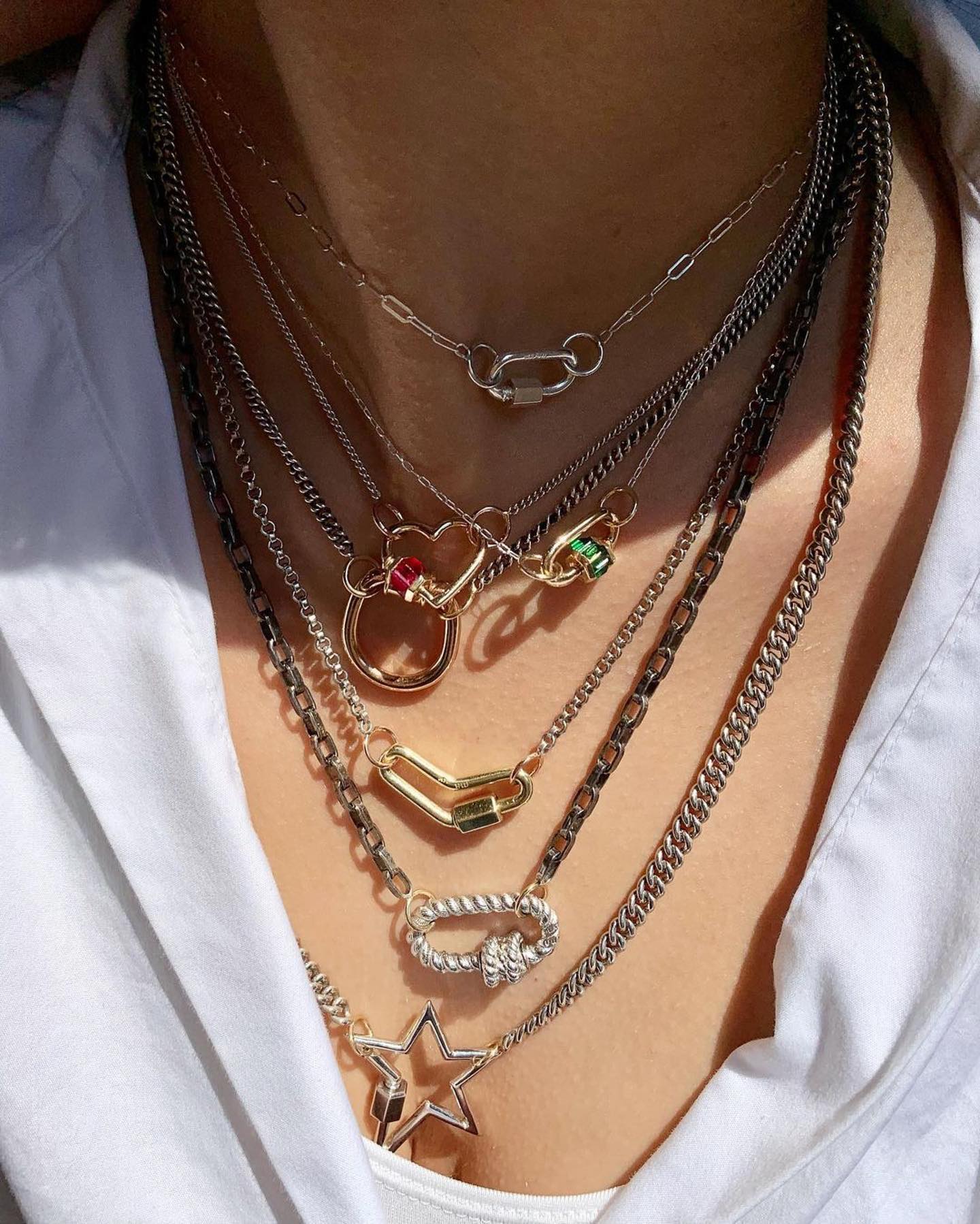 Close up of woman's decolletage wearing many necklaces including silver rolo chain