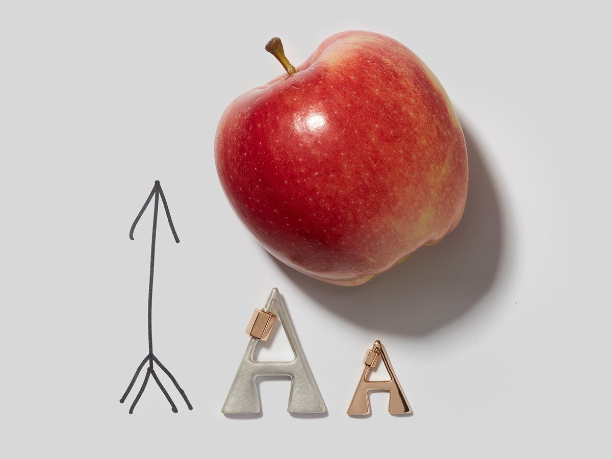 Large silver letter A charm and small rose gold letter A charm alongside an apple and an arrow