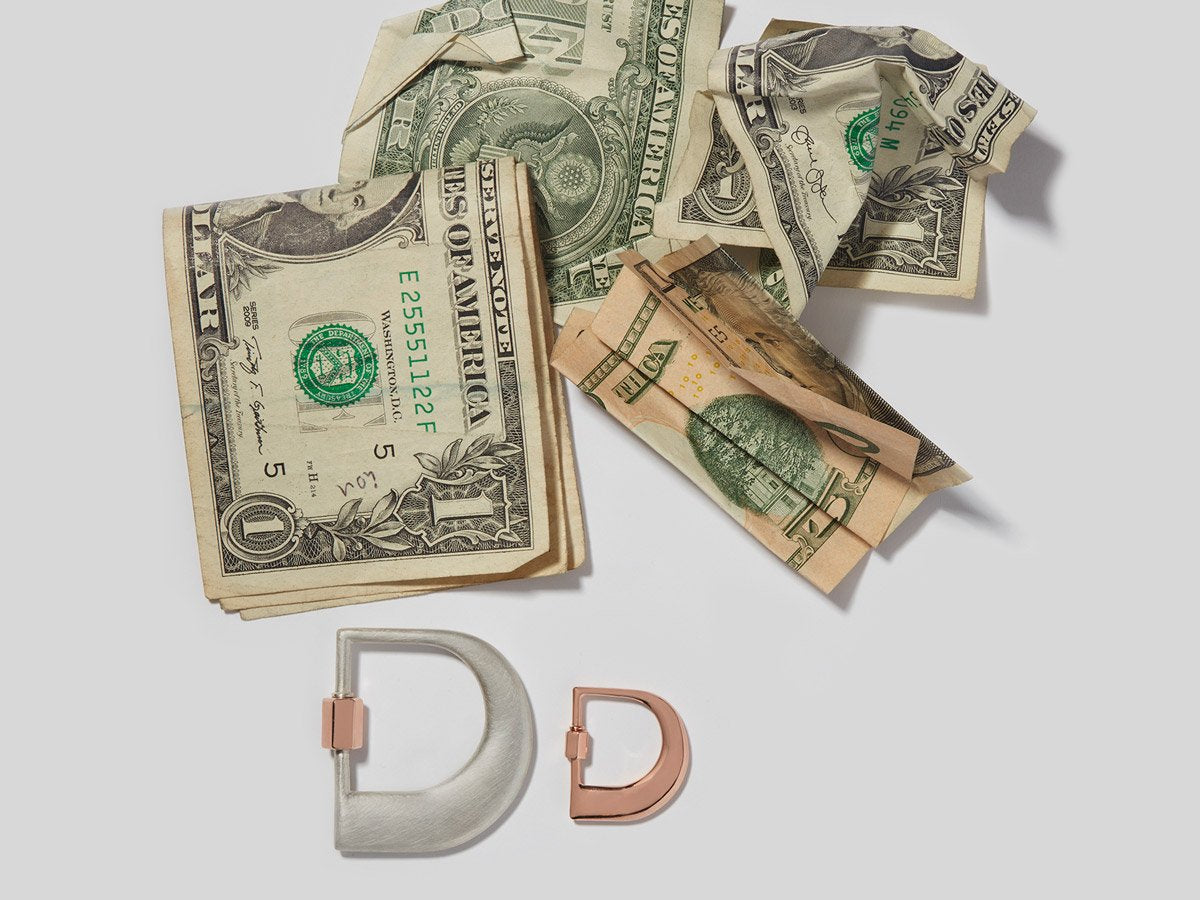 Large silver letter D charm and small rose gold letter D charm alongside a dollar bills