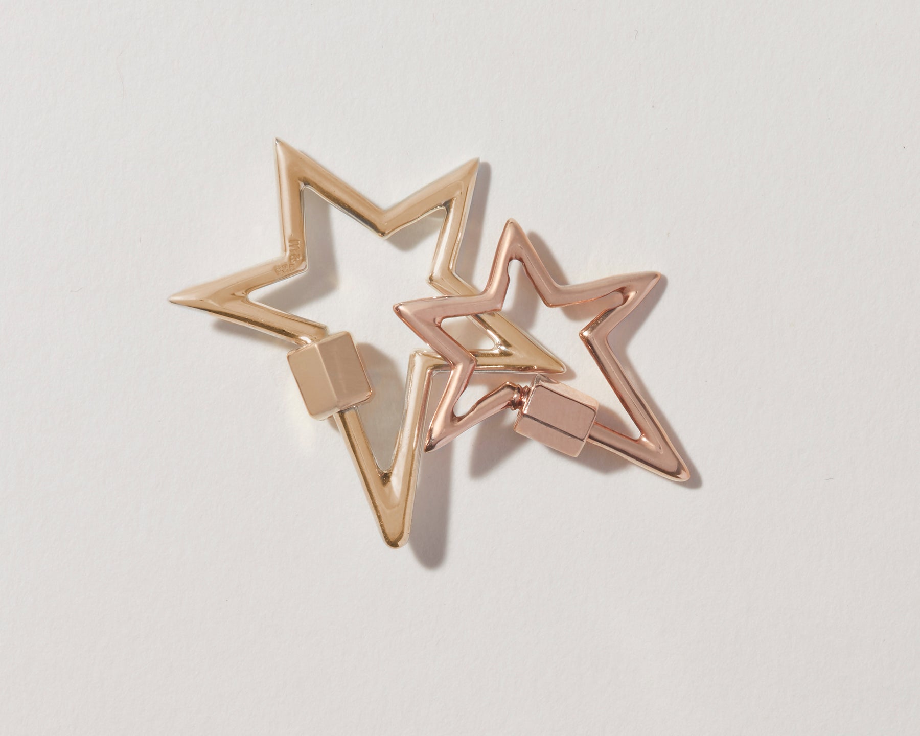 Big gold star charm and small rose gold star charm against gray backdrop