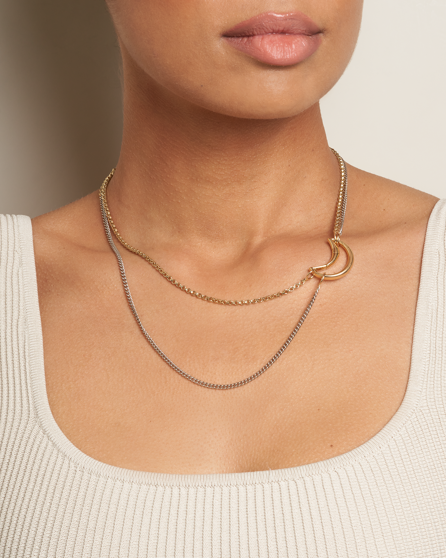Close up of woman's decolletage wearing gold and silver two tone chain necklace with moon charm on the right side