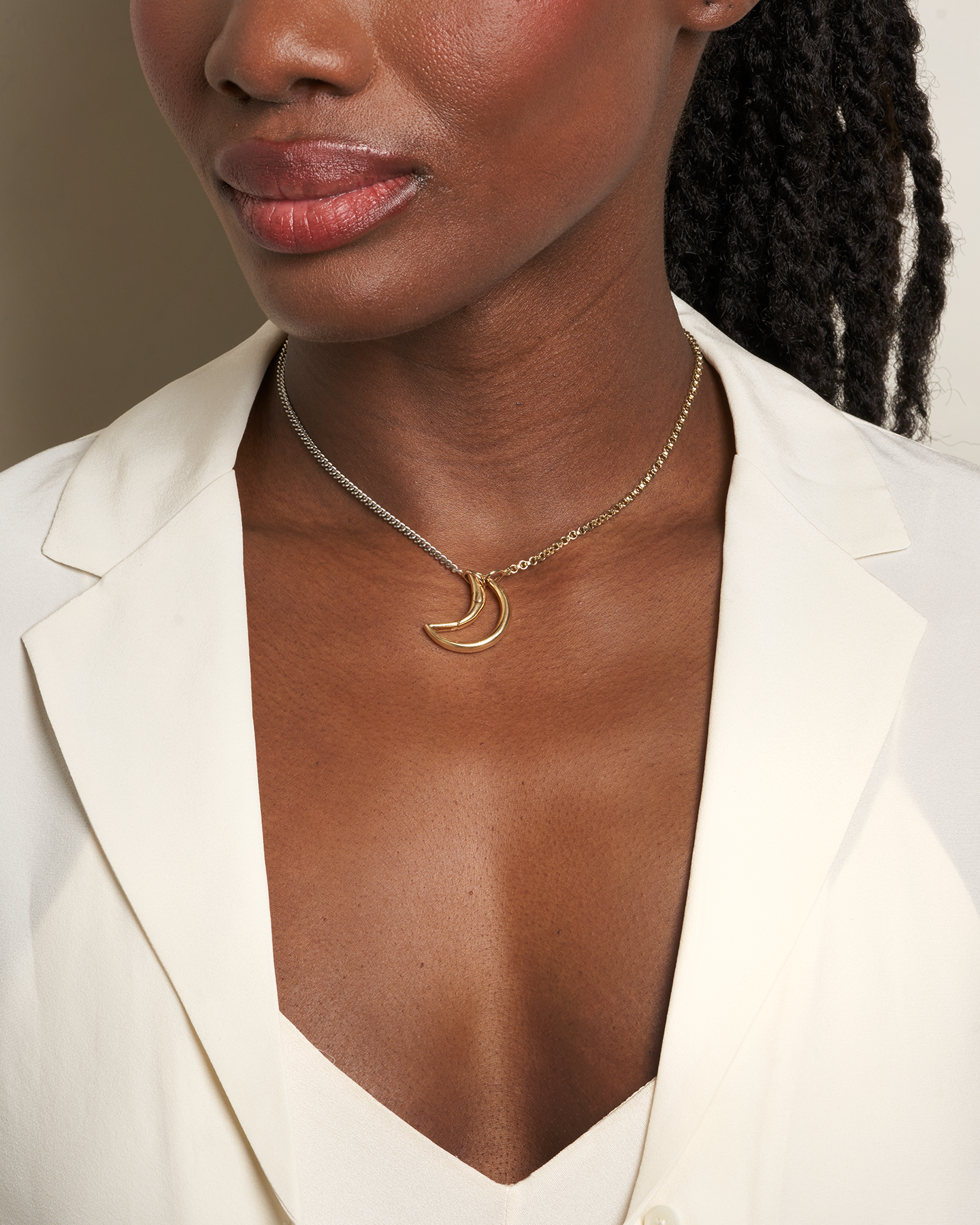 Close up of woman's decolletage wearing necklace with moon lock charm on two-tone chain