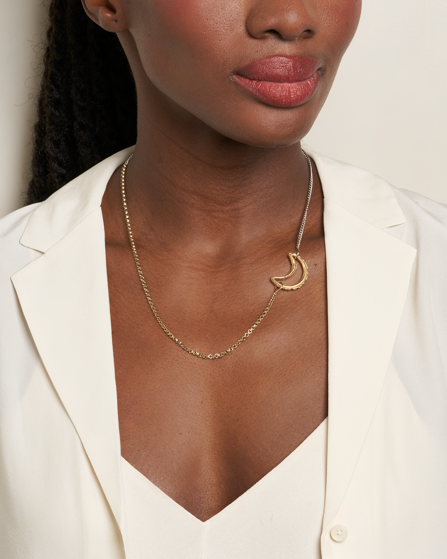 Close up of woman's decolletage wearing long gold and silver two tone chain necklace with moon charm on the right side