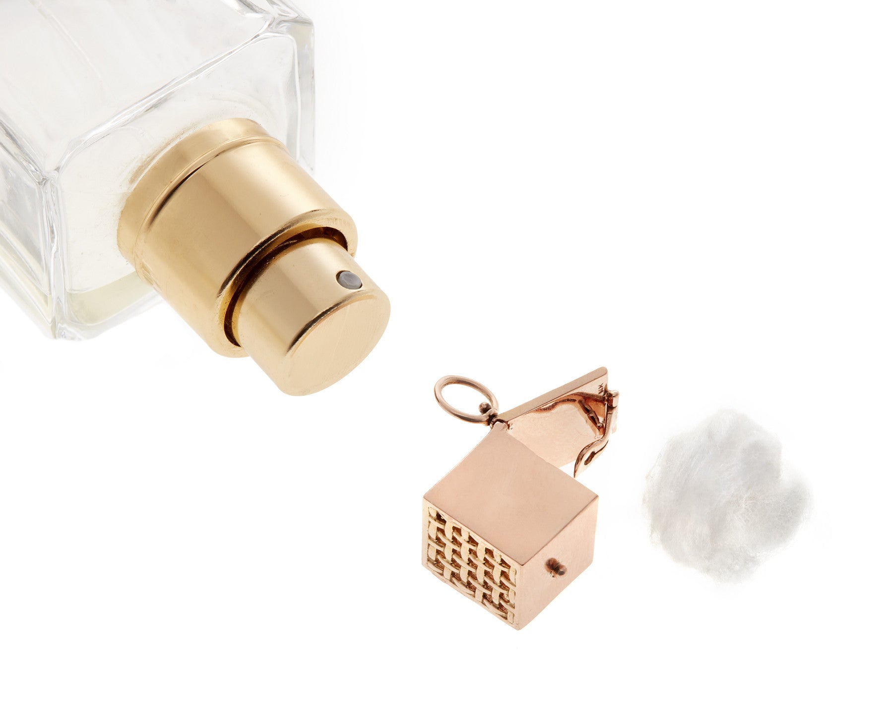 Rose gold vinaigrette vessel with top open alongside cotton ball and top section of fragrance bottle against white backdrop